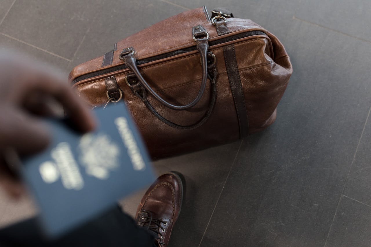 menu-11 Brown leather bag with passport in an airport setting, ideal for travel and fashion themes.