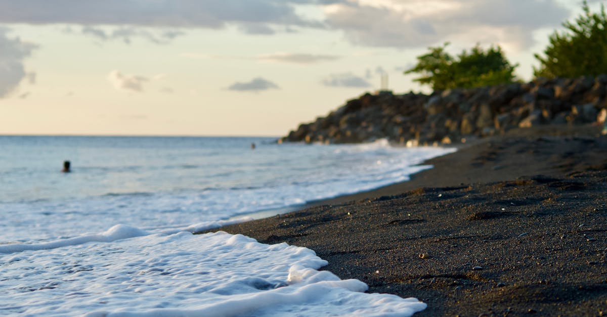 Calm ocean waves on a black sand beach in Guadeloupe with a serene sunset backdrop.