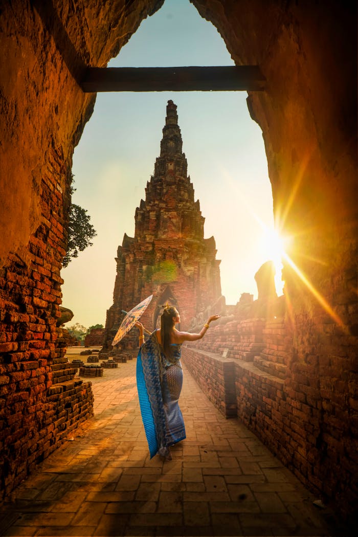 about-02 A woman in traditional wear stands with an umbrella at a historic Ayutthaya temple during sunset.