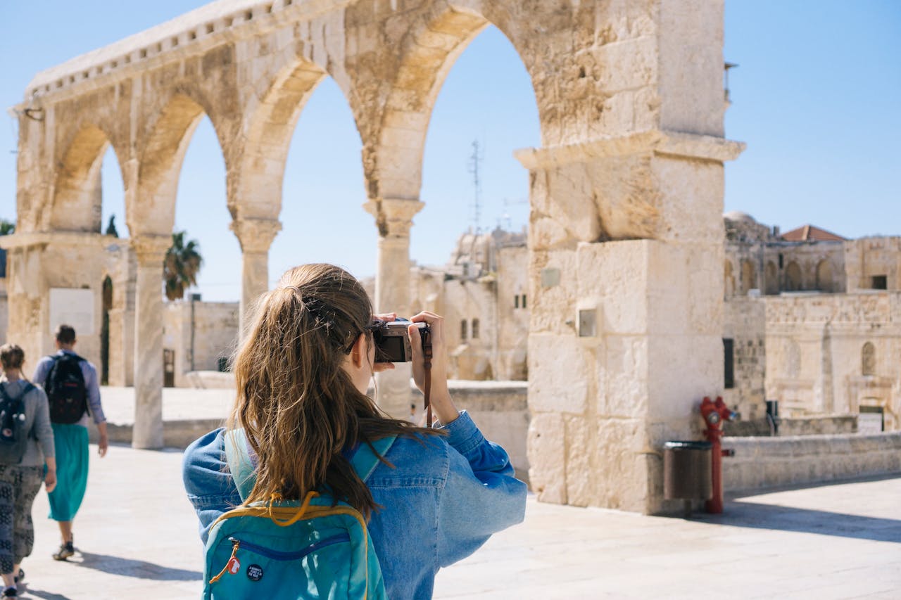 menu-01 A tourist photographs the ancient stone arches in Jerusalem's Old Town, capturing the essence of travel and history.