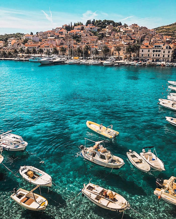 menu-13 Boats in the vibrant blue waters of Hvar, Croatia, showcasing a charming coastal town under sunny skies.