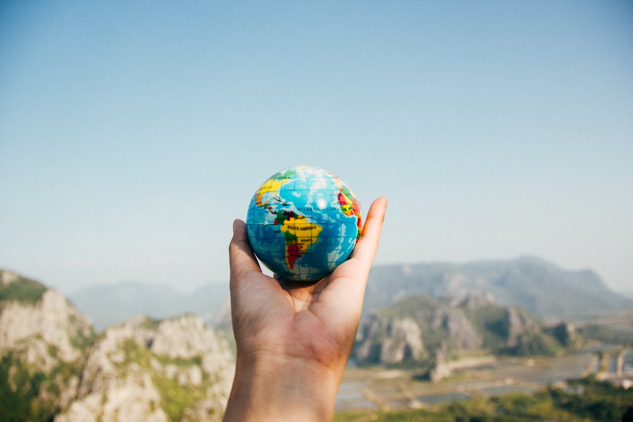 menu-03 Hand holding a globe against a mountain background symbolizing travel and exploration.