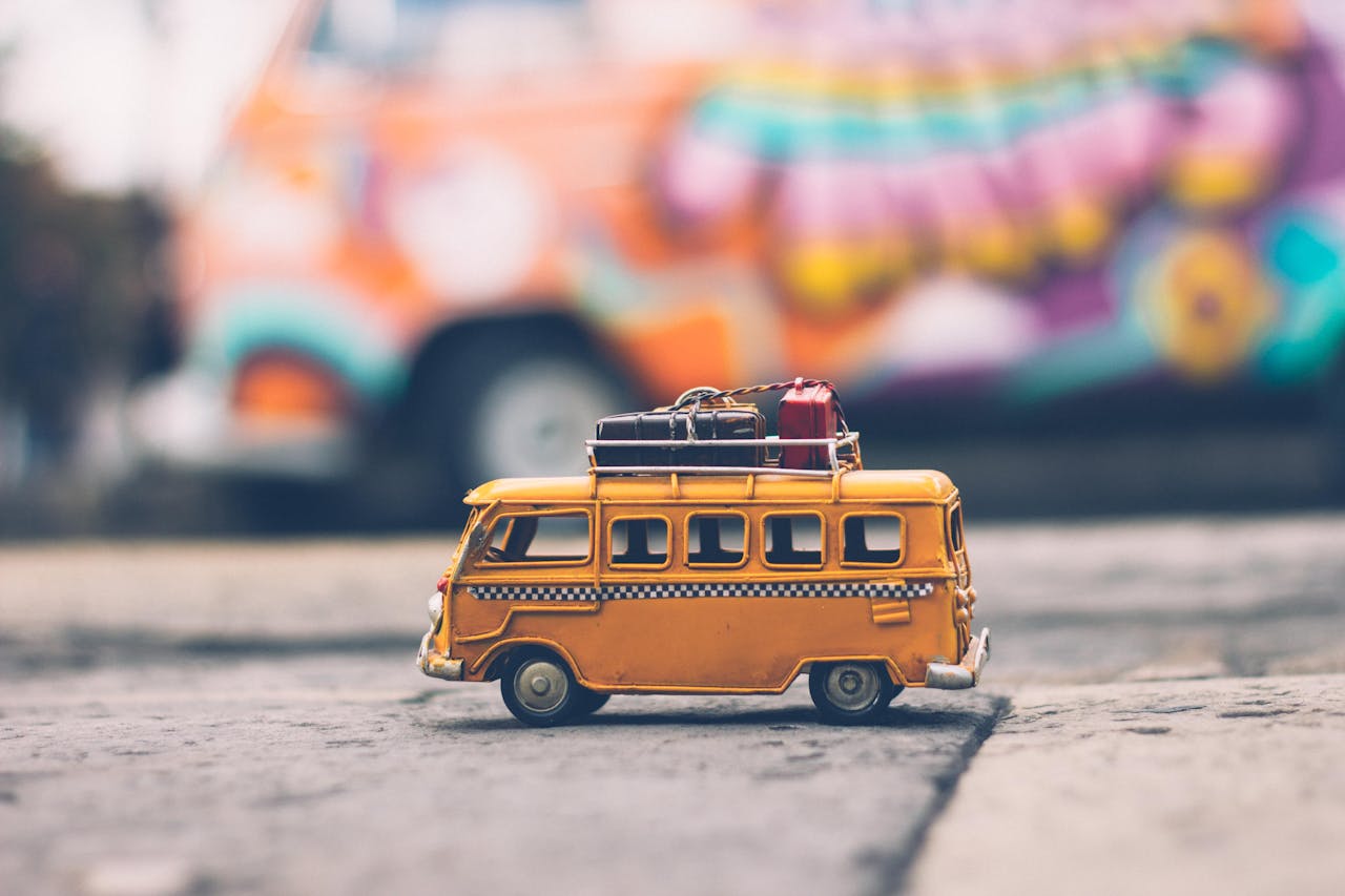 menu-06 Close-up of a toy Volkswagen van with luggage, set against a colorful street backdrop, evoking summer travel vibes.