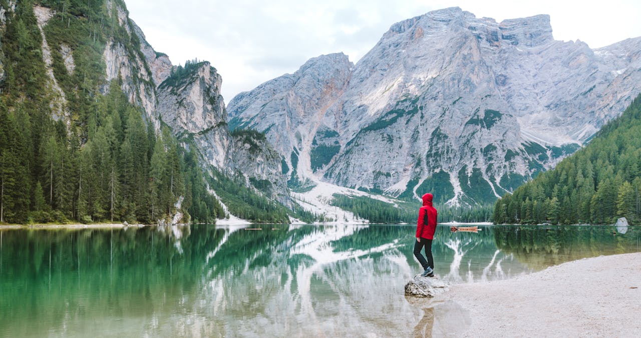menu-01 Person standing by the scenic Lake Braies with majestic Dolomite mountains reflected in the water.